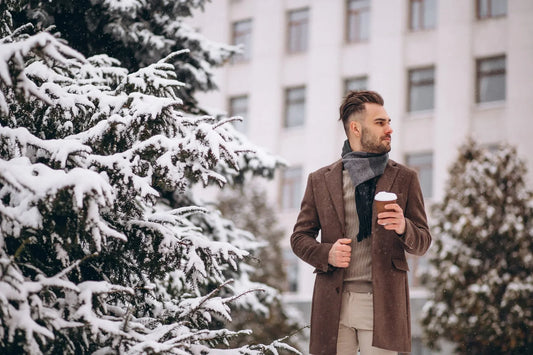 Mann mit elegantem Wintermantel und Schal im Schnee; klarer, stilvoller Look für kalte Tage.