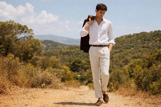 Junger Mann mit weißem Hemd und beigefarbener Stoffhose in sommerlicher Naturkulisse – minimalistisches, elegantes Outfit im Old-Money-Stil.
