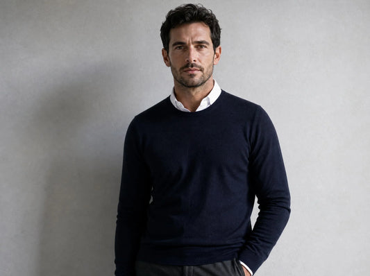 Mann Mitte dreißig in marineblauem Rundhalspullover über weißem Hemd mit Kent-Kragen: klassische Pullover-Hemd-Kombination für den Herbst aus der Huberd Herbstkollektion