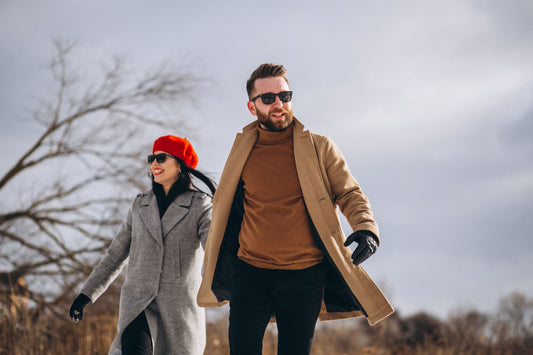 Junges Paar in eleganten Mänteln in neutralen Farben spaziert im Winterpark – Beispiel für minimalistisches Outfit und Qualitätskleidung von Huberd